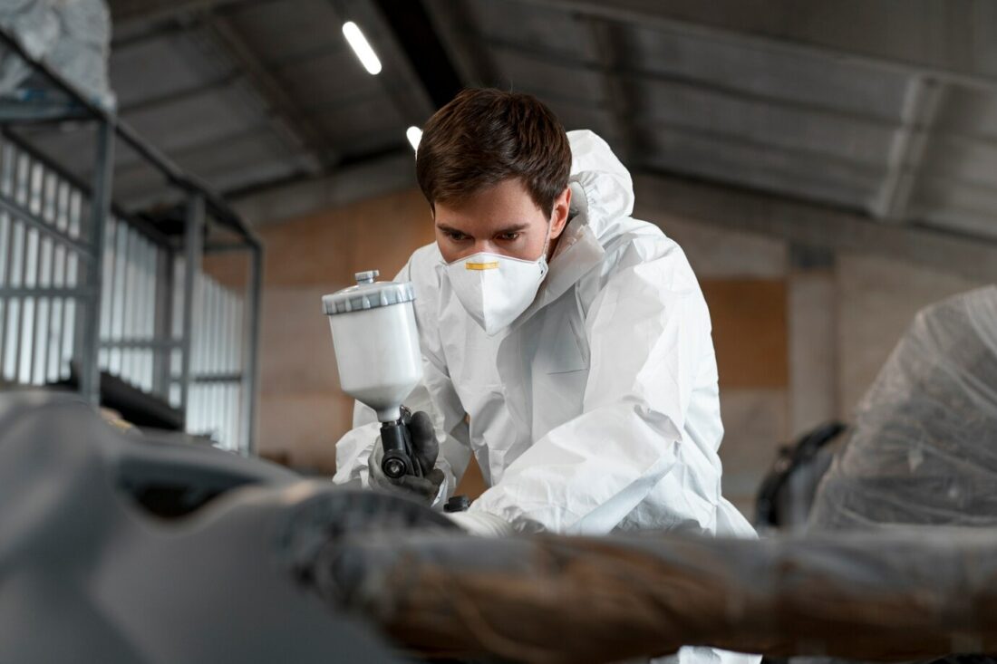 Homme en costume de protection avec un masque qui tient un pistolet à peinture dans un atelier